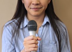 Woman's nose, mouth and chest with a hand holding a microphone in front of her