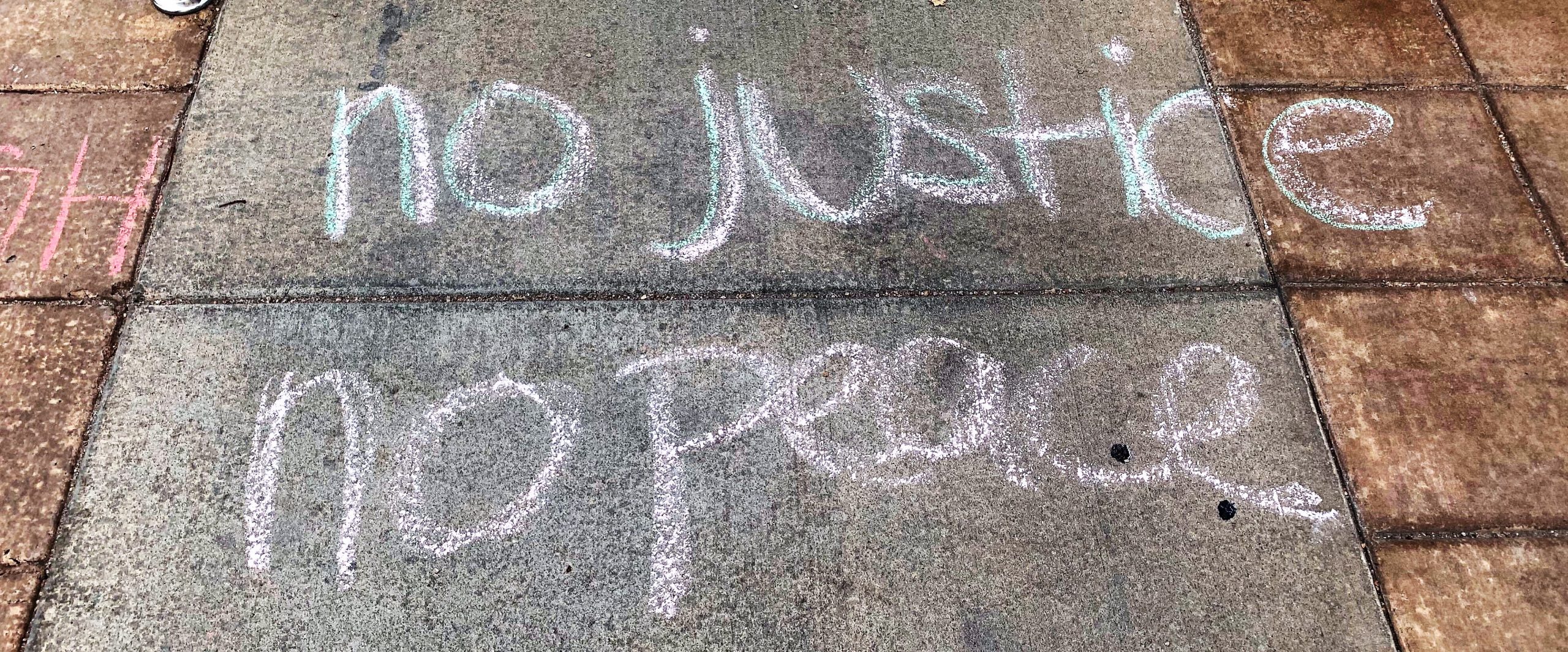 Chalk writing on sidewalk that says "no justice no peace"